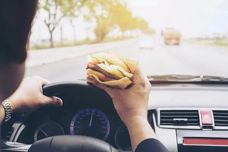A person driving a car while eating a hamburger