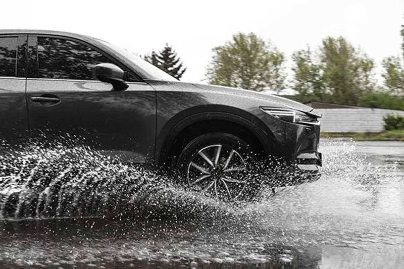 A black SUV driving through water on a wet road